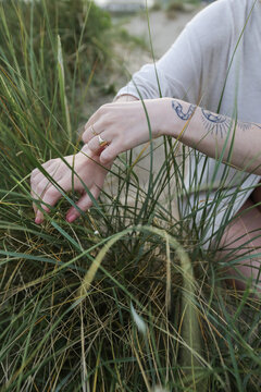 Young woman with tattoo touching grass softly.