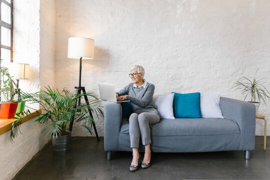 Senior businesswoman sitting at the couch in the office using her laptop