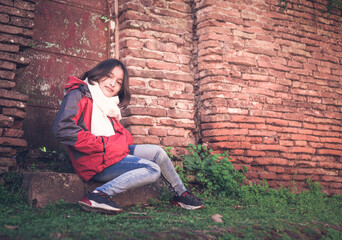 niña adolescente posando sentada en escalo de puerta antigua con fondo de ladrillos deteriorados en pueblo rural