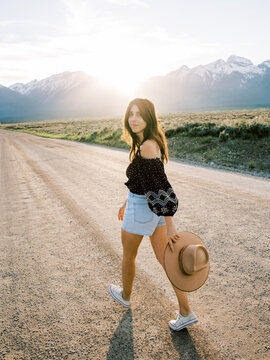 Woman looking at camera walking on dirt road at sunset 