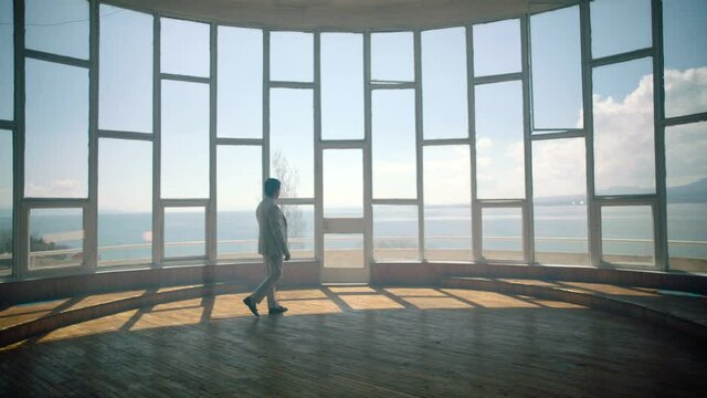 Businessman in a suit is walking towards a big window that looks at the sea . Back View of the Businessman wearing a Suit Standing in empty place . Shot on ARRI ALEXA cinema camera in slow motion .