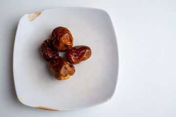 Arabic food dates are placed on a white plate on a white background photographed with overhead style