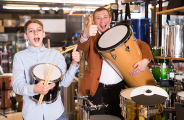 young russian father and teenage son examining drum units in guitar shop