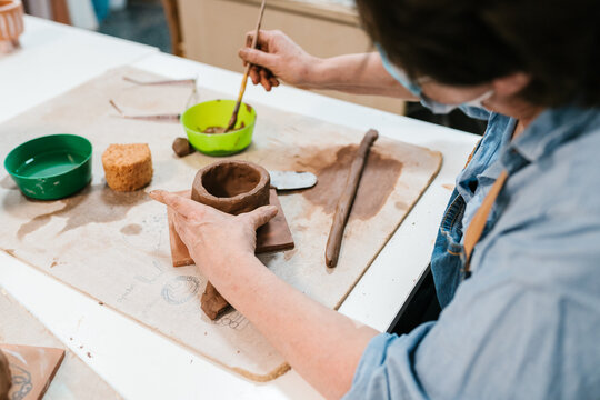 Crop woman making pot from clay on table