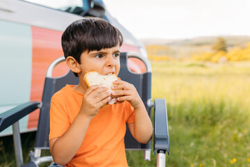Child eating delicious sandwich in armchair on lawn