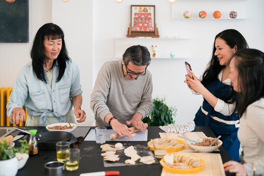 Cheerful woman taking photo of Asian friends cooking gyoza for lunch
