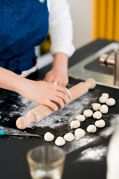 Anonymous woman rolling raw dough at table in kitchen