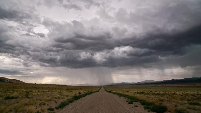 Timelapse of rainstorm looking down dirt road into the desert landscape of Utah during monsoon thunderstorm.