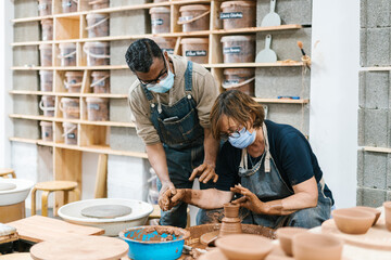 Black man teaching woman to craft clay vase