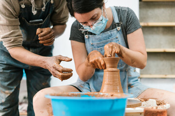 Crop male potter watching apprentice making pot
