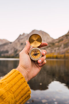 Unrecognizable person holding a compass besides a lake