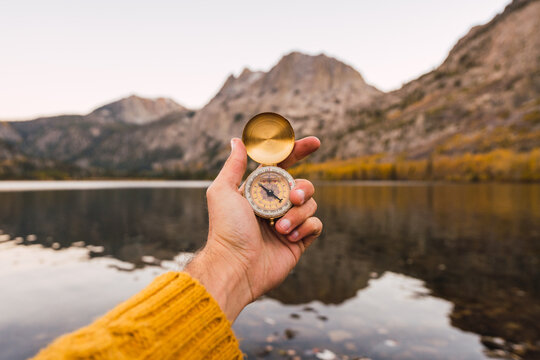 Unrecognizable person holding a compass besides a lake