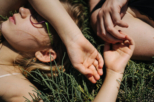 Hands of mother and child who lie on green grass