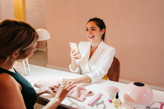 Happy woman using smartphone and speaking with manicurist