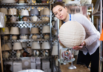 Happy smiling girl is choosing modern table lamp in furniture store..