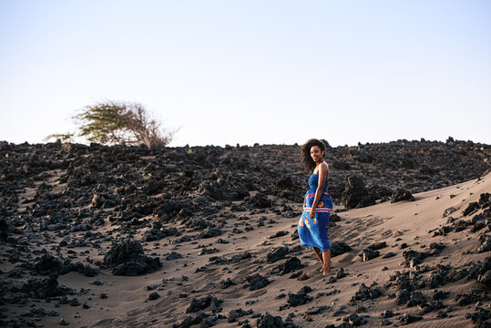 African woman standing on volcanic sand dune on beach