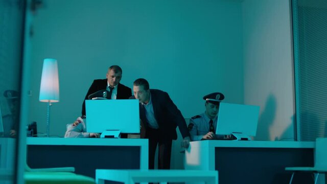 Police detectives working together in computer room to try and solve a case . Men at desk in room with data on screens .  Staged shot with fictional uniforms, so property release not required .