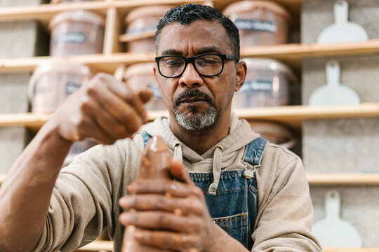 Black male artisan spilling water on clay vessel