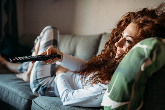 Woman in pajamas lying down on the couch watching tv