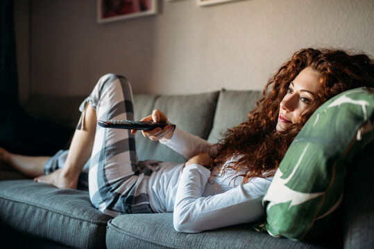 Woman in pajamas lying down on the couch watching tv
