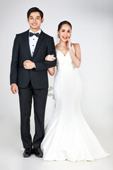 Young attractive Asian couple, bride and groom, woman wearing white wedding dress. Man wearing black tuxedo, standing arm in arm together in black and white. Concept for pre wedding photography