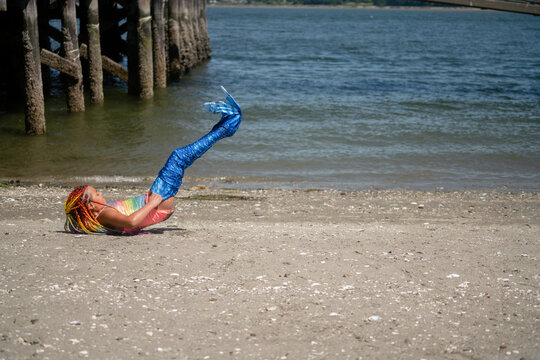 Girl on sandy beach puts on mermaid tail swimsuit
