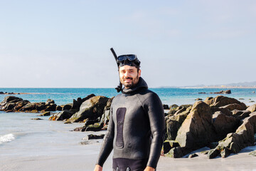 young latin man with a wetsuit and snorkel on the rocky  beach