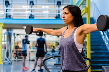 young hispanic latina woman in a gymnasium doing lateral weightlifting