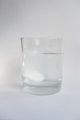 glass with water and white effervescent tablet on a white background