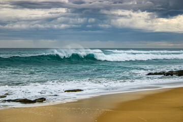 Turquoise wave crashing on beach set against an angry stormy sky
