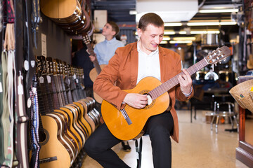 .Male visitor examining various acoustic guitars in musical shop