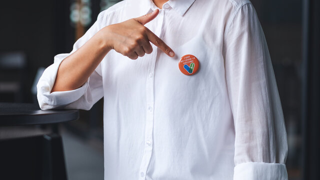 Closeup image of a woman showing and pointing finger at Covid-19 vaccinated sign brooch on shirt