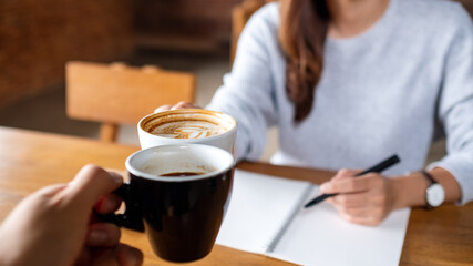 Closeup image of a couple people clinking coffee cups while working together