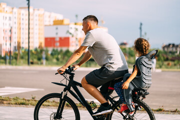 The father rides on a bicycle small daughter in a children's seat