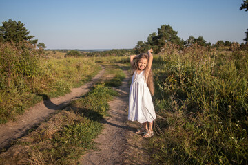 Fototapeta na wymiar Little happy girl in a white dress runs on rural roads, childrens tourism, school holidays. 