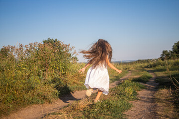 
Little happy girl in a white dress runs on rural roads, childrens tourism, school holidays.
