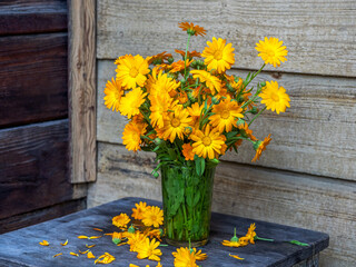 Summer bright bouquet of orange calendula in a glass glass on a stool