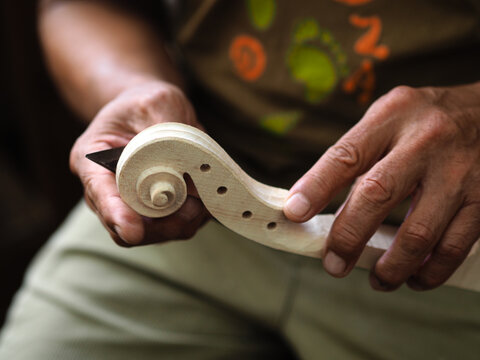 Luthier carving a classic violin head and curl with a small knife in his wrinkled hands - Powered by Adobe