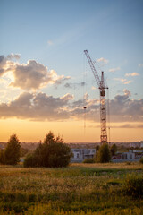 Fototapeta na wymiar A construction site with a high-rise block under construction in an urban environment dominated by a large industrial crane, silhouetted against a beautiful cloudy sunset. construction landscape