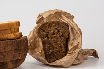 Slices of rye and wheat bread are laid out on a white background. Wrap half a loaf of dark bread in brown paper. Isolated