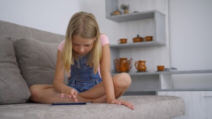 A school-age girl is at home and uses a tablet computer to play and draw. Remote training without leaving home. Development of abilities in children.