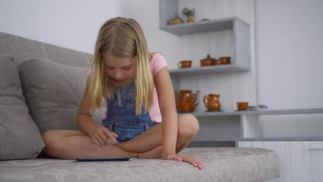 A school-age girl is at home and uses a tablet computer to play and draw. Remote training without leaving home. Development of abilities in children.