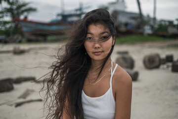 Close up portrait of beautiful young mongol woman in white dress, blurred background. Brunette long curly hair. Looking at camera with copy space. Romantic portrait. Wind in her hair.