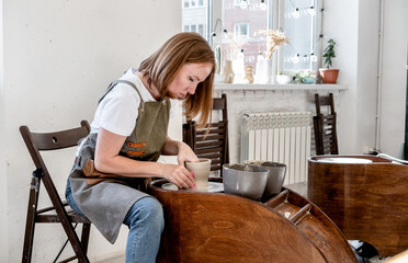 Woman working on the potter's wheel. Ceramist young woman making clay product on pottery lathe in studio