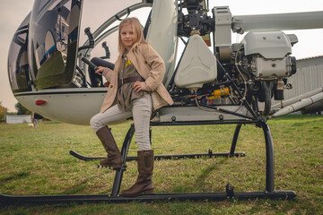 Blond preteen girl posing near open helicopter on flying field