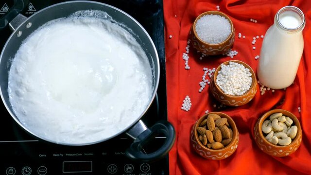 Milk is being boiled in a pan over a gas stove to prepare Sago / Sabudana Kheer. Indian dessert . Almonds  sugar  cashew nuts  and white tapioca pearls in the kitchen - Sabudana Kheer ingredients