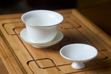 Gaiwan on chaban selective focus. Tea ceremony gong fu cha. Chinese white pottery Dehua white Chinese porcelain gaiwan bowl tea cup and lid plate with gold border on bamboo teaboard tea tray chaban
