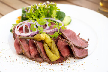 Roast beef slices with pepperoni, onions and salad on a white plate, copy space, selected focus