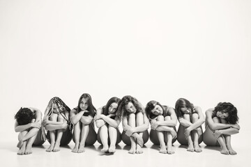 Naklejka premium Girls with different types in one photo. The girls sit on the floor and hug themselves by the legs. A place for a text on female psychology. Understanding Female Psychology