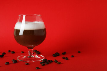 Glass of irish coffee and coffee seeds on red background